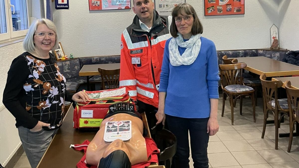 Hanne Angenendt, Holger Sauer und Silvia Schüßler stehen lächelnd um einen Tisch. Auf diesem ist die Erste-Hilfe-Tasche LifeBag und eine Beatmungspuppe.