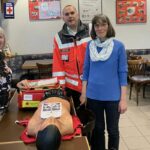 Hanne Angenendt, Holger Sauer und Silvia Schüßler stehen lächelnd um einen Tisch. Auf diesem ist die Erste-Hilfe-Tasche LifeBag und eine Beatmungspuppe.