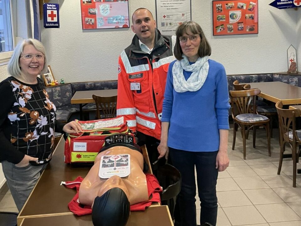 Hanne Angenendt, Holger Sauer und Silvia Schüßler stehen lächelnd um einen Tisch. Auf diesem ist die Erste-Hilfe-Tasche LifeBag und eine Beatmungspuppe.