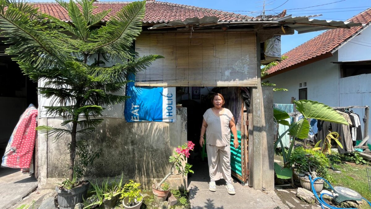 Widiani steht vor ihrem Wäscheservice in Denpasar, Bali, neben Wäsche und Pflanzen.