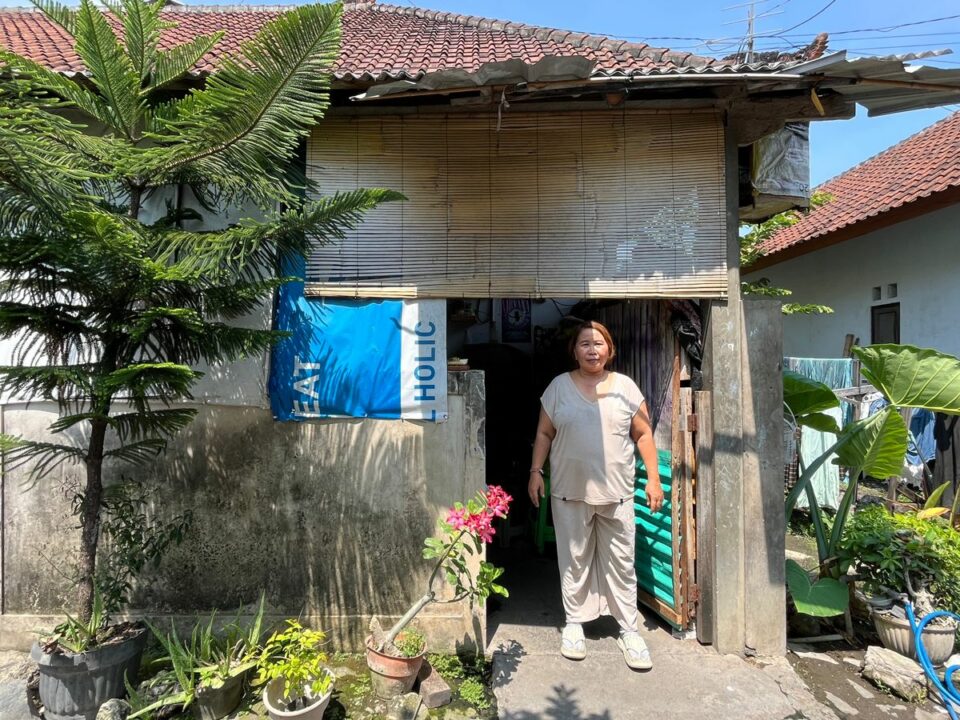 Widiani steht vor ihrem Wäscheservice in Denpasar, Bali, neben Wäsche und Pflanzen.