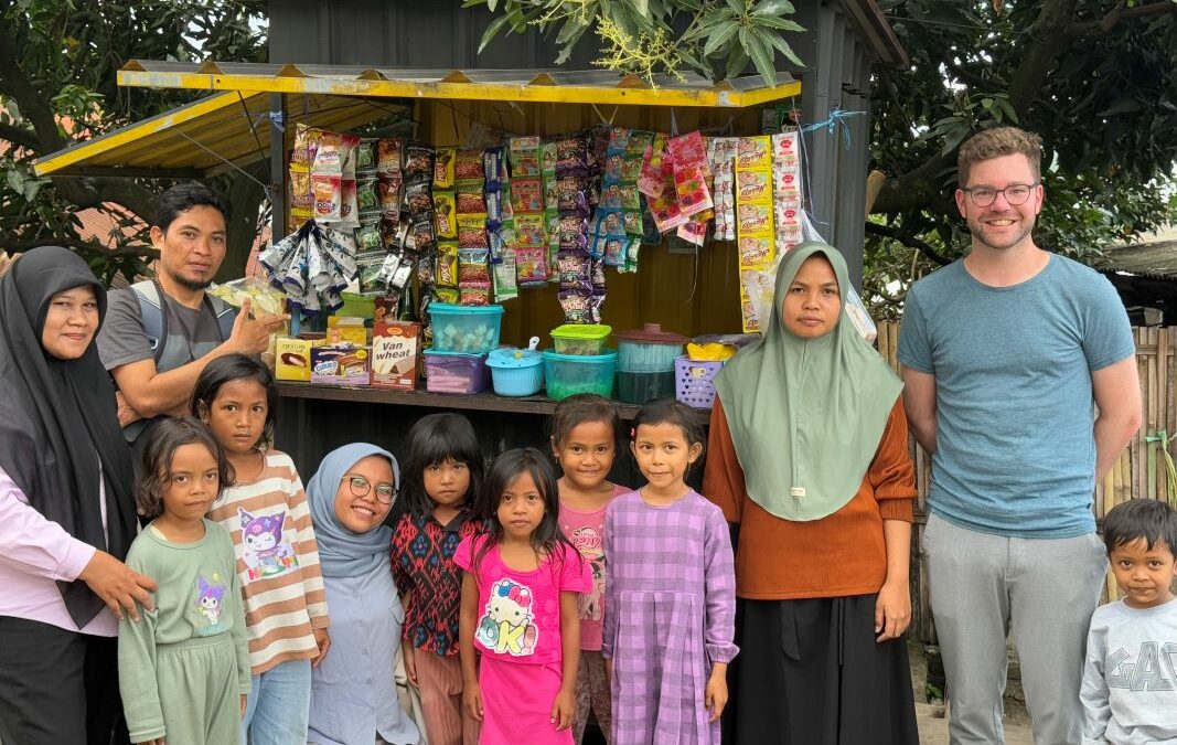 Gruppenbild vor einem kleinen Verkaufsstand in Jineng mit Kleinstunternehmerin, Kindern, Team von Global Micro Initiative e.V. und Tobias Schüßler.