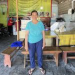 Kleinstunternehmerin steht in ihrem Imbiss-Stand und lächelt in die Kamera.