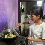 Erna frittiert Bananenchips in einem Wok auf ihrem kleinen Gaskocher.