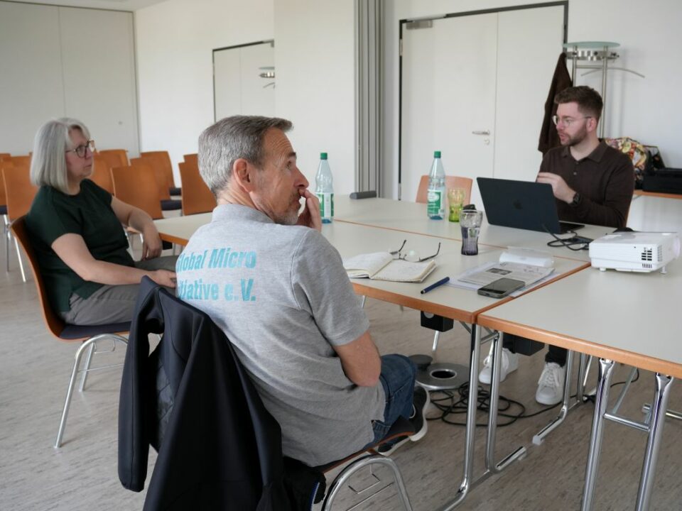 Die Vorstandsmitglieder Achim, Silvia und Tobias sitzen an einem großen Tisch. Vor Tobias steht ein aufgeklappter Laptop.