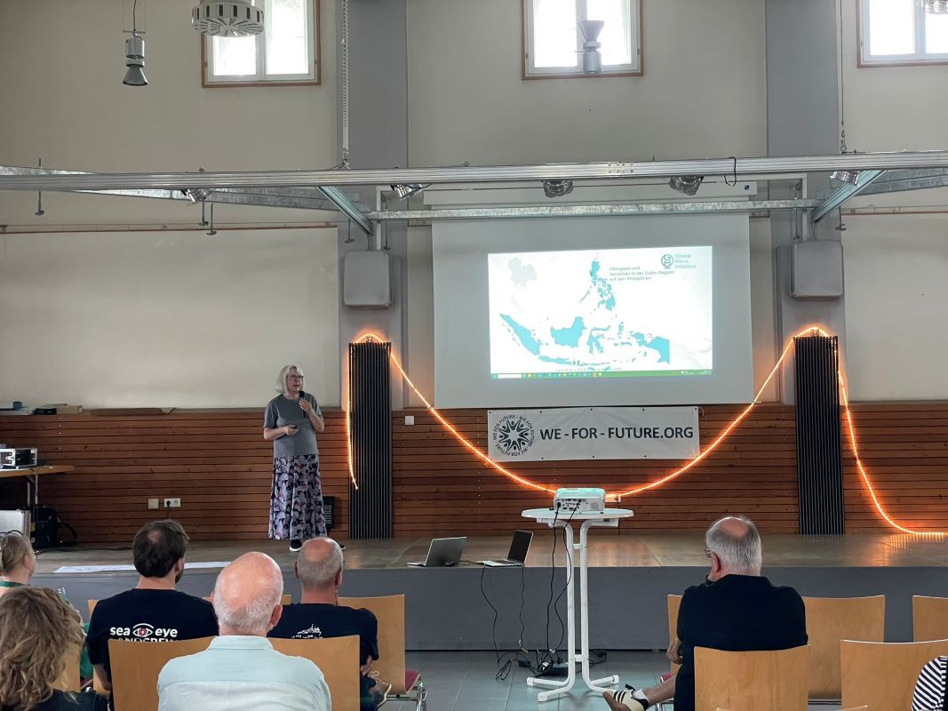 Vorstandsmitglied Silvia Schüßler berichtet in einer Präsentation auf einer Bühne über die Arbeit von Global Micro Initiative e.V.