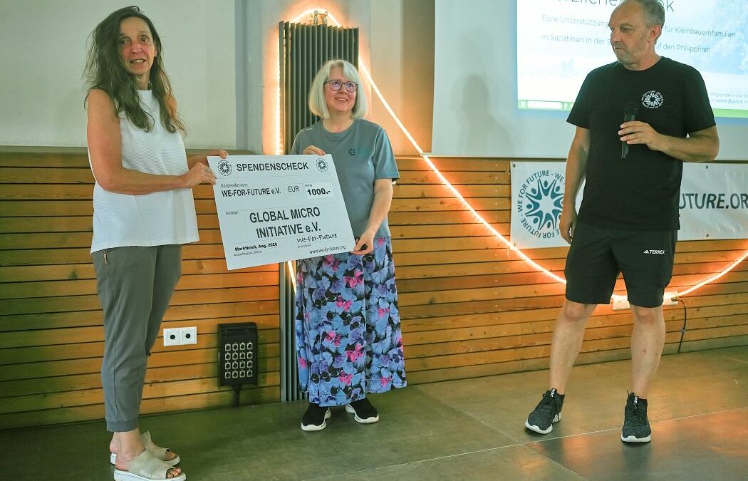 Eine Frau überreicht Silvia von Global Micro Initiative e.V. einen Spendenscheck über 1.000 Euro von WE-FOR-FUTURE e. V.